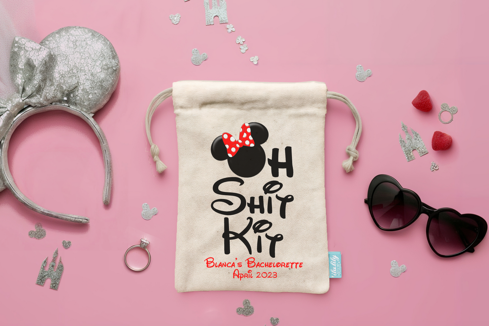 Decorative bag with 'Oh Shit Kit' design, silver Minnie Mouse ears, sunglasses, and heart-shaped decorations on a pink background.